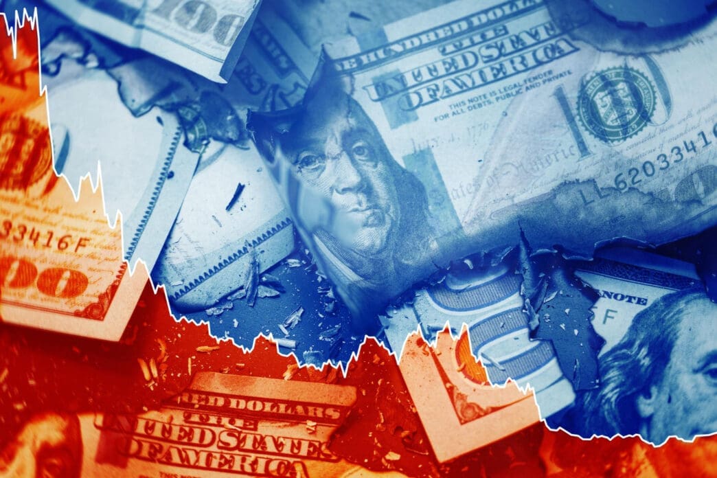 A conceptual image of damaged and burning US hundred-dollar bills with a white line graph showing a downward trend overlaid on top.