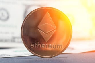 A physical Ethereum coin stands on its side in front of a blurred U.S. dollar bill