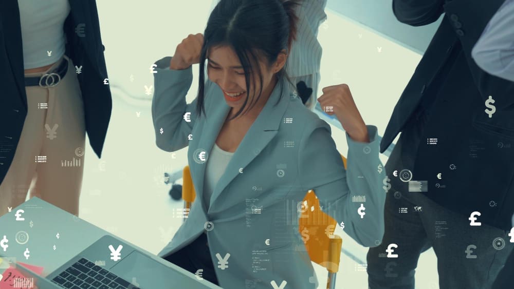 An excited businesswoman with raised fists celebrates financial success in an office, with currency symbols and data graphics overlaid on the image.