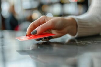 A close-up shot of a hand with dark nail polish, placing a red card on a dark, reflective counter.