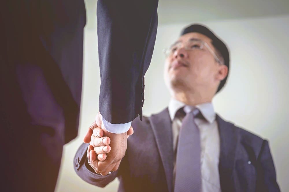 A close-up, low-angle shot of two businesspeople in suits shaking hands.