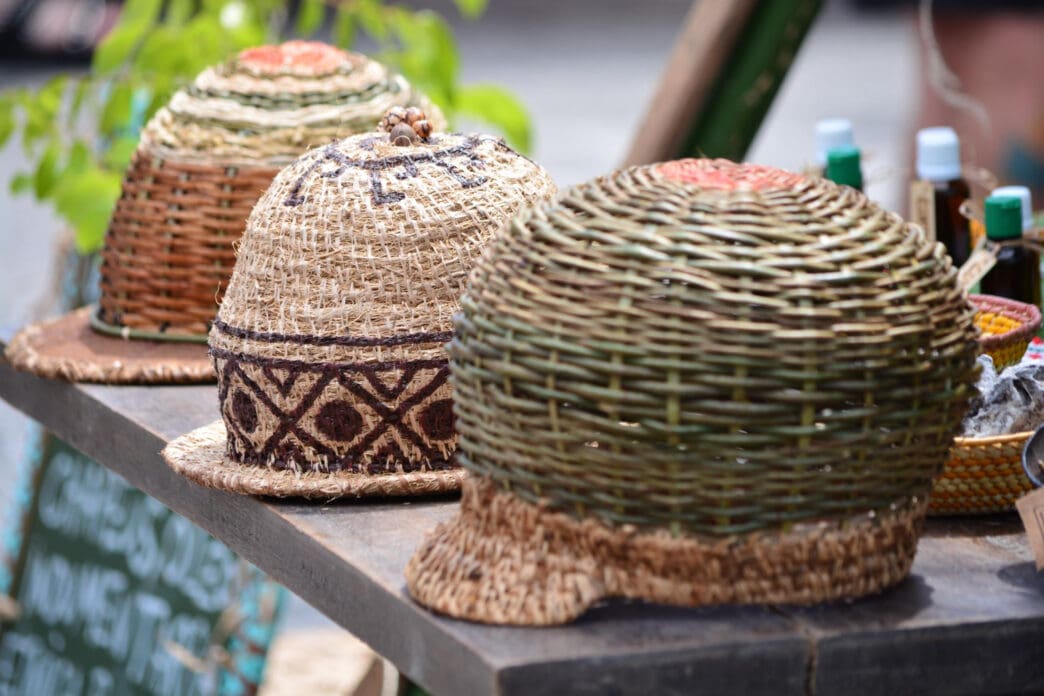 Three hand-woven, beehive-shaped hats are displayed on a wooden table
