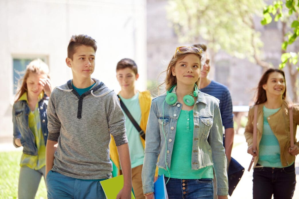 A group of diverse and happy high school students, including a boy and a girl in the foreground, walking together outdoors on a campus.