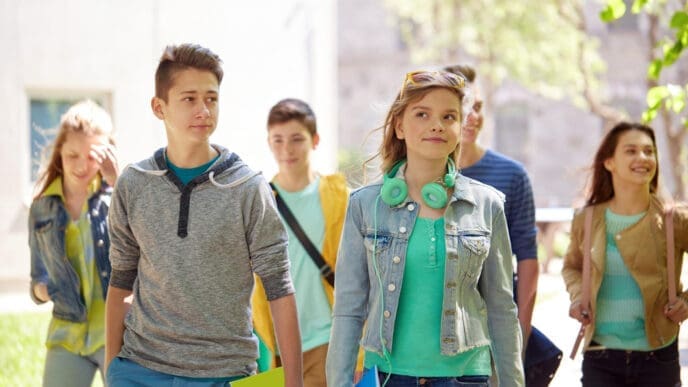 A group of diverse and happy high school students, including a boy and a girl in the foreground, walking together outdoors on a campus.