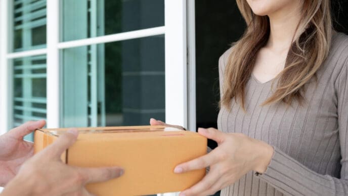 A smiling woman receives a brown cardboard package from a delivery person's hands.