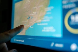 A passenger's finger touches an LCD entertainment screen on a plane, which displays a map of Brazil with an icon of a plane over the coast near São Paulo.