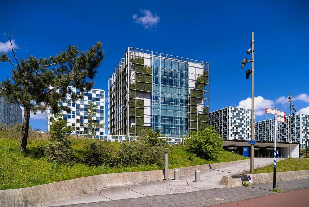 The International Criminal Court building complex in The Hague, Netherlands, a modern structure with glass and green plant-covered facades on a sunny day.