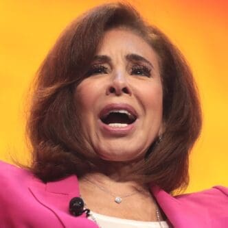A close-up portrait of Jeanine Pirro speaking, with her mouth open and a dynamic expression, wearing a pink blazer in front of a bright orange background.