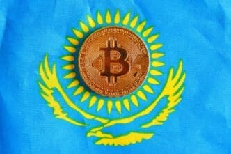 A golden Bitcoin coin is placed on the national flag of Kazakhstan, which is blue with a golden sun and eagle.