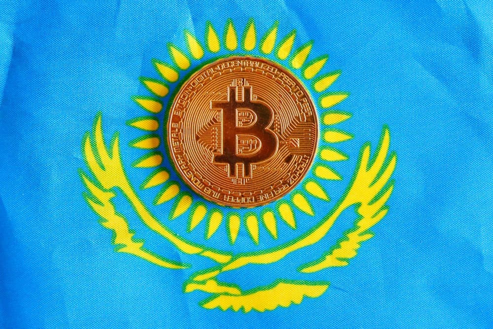 A golden Bitcoin coin is placed on the national flag of Kazakhstan, which is blue with a golden sun and eagle.