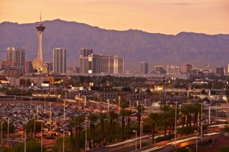 An aerial view of the Las Vegas skyline at sunset, with the Stratosphere tower and a mountain range in the background.