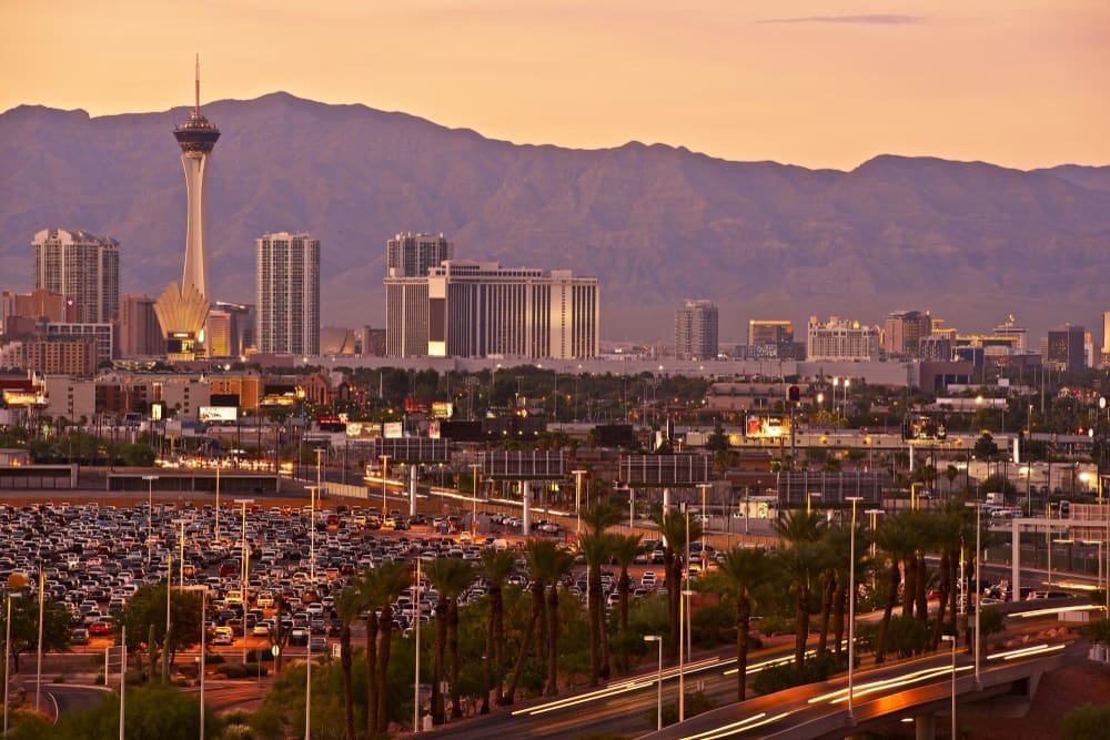 An aerial view of the Las Vegas skyline at sunset, with the Stratosphere tower and a mountain range in the background.
