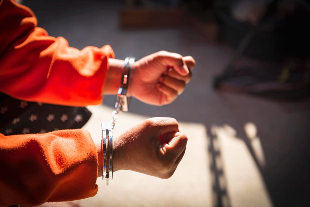 A close-up shot of a person's hands in handcuffs, wearing an orange jumpsuit.