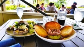 A restaurant table with two plates of food, one with a sandwich and salad, and another with a seafood tartare and fried taro.