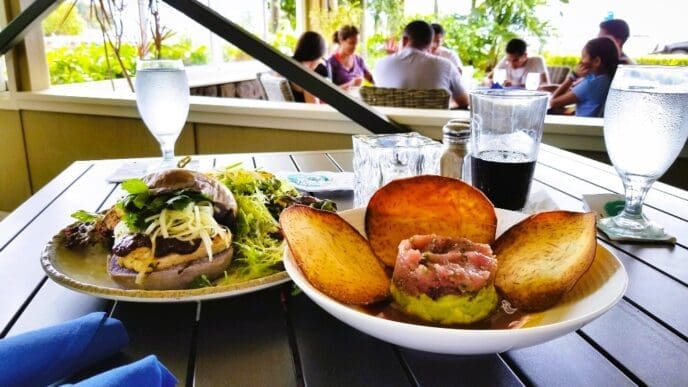 A restaurant table with two plates of food, one with a sandwich and salad, and another with a seafood tartare and fried taro.
