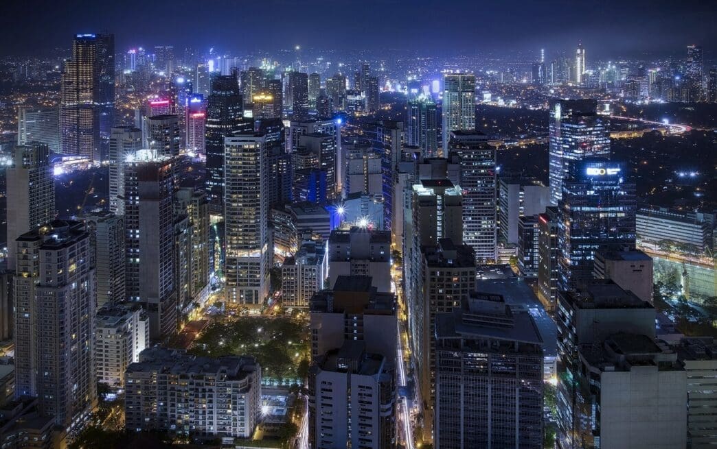 A panoramic night view of the dense urban skyline of Makati City, with all the skyscrapers and streets illuminated by countless lights.
