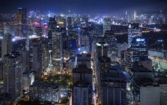 A panoramic night view of the dense urban skyline of Makati City, with all the skyscrapers and streets illuminated by countless lights.