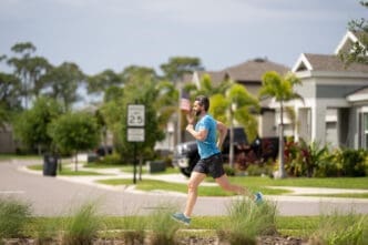 A fit man with a beard is running on a street in a suburban neighborhood.