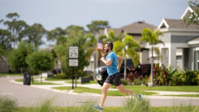 A fit man with a beard is running on a street in a suburban neighborhood.