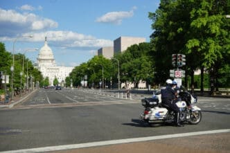 Two Metropolitan Police officers on a motorcycle are positioned on Pennsylvania Avenue in Washington, D.C., with the U.S. Capitol Building in the distance.