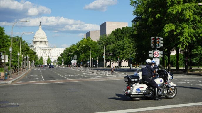 Two Metropolitan Police officers on a motorcycle are positioned on Pennsylvania Avenue in Washington, D.C., with the U.S. Capitol Building in the distance.