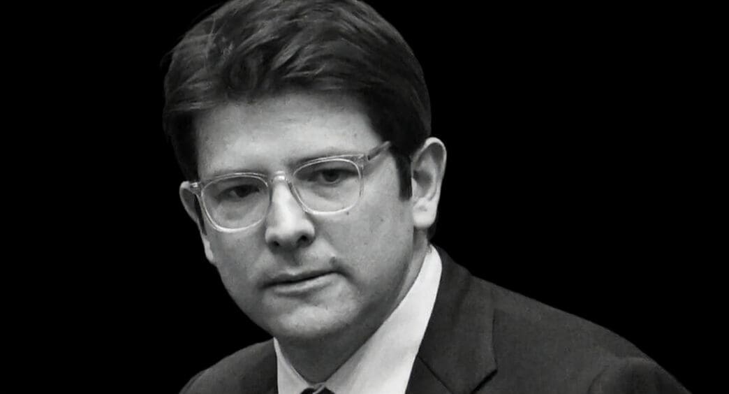 A black and white portrait of Miguel Uribe Turbay, a politician with glasses, wearing a suit and looking to the side with a serious expression.