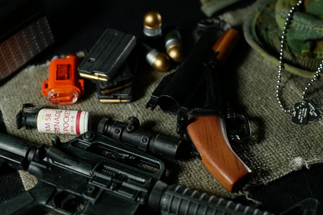 A collection of military equipment, including a rifle, a pistol, grenades, and ammunition, on a piece of cloth.