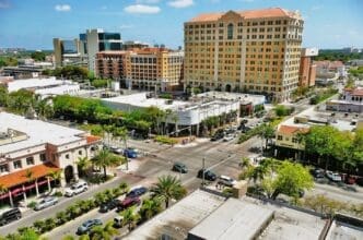 An aerial view of Miracle Mile in Coral Gables, Florida, showing a busy street intersection with Mediterranean-style buildings and palm trees.