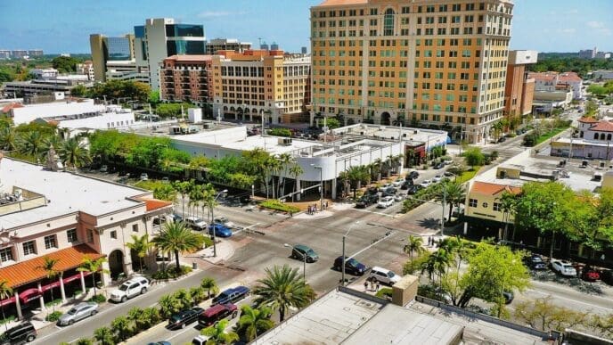 An aerial view of Miracle Mile in Coral Gables, Florida, showing a busy street intersection with Mediterranean-style buildings and palm trees.