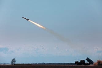 A ground-launched missile soars into the sky from a military vehicle, leaving a fiery trail