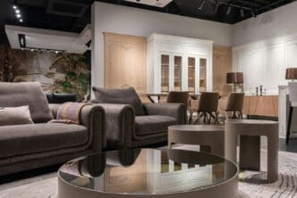 A photograph of a modern, stylish living room with a gray sofa and a round glass coffee table, and a dining area with a large cabinet in the background.