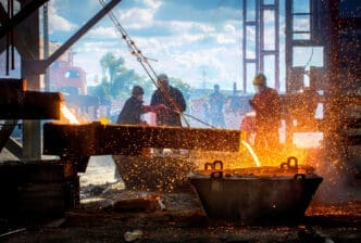 A group of industrial workers in a foundry are pouring molten metal, creating a bright stream of liquid and a shower of sparks in a dark, dramatic scene.