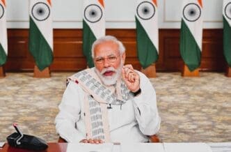 Indian Prime Minister Narendra Modi speaks while seated at a desk, with Indian flags in the background