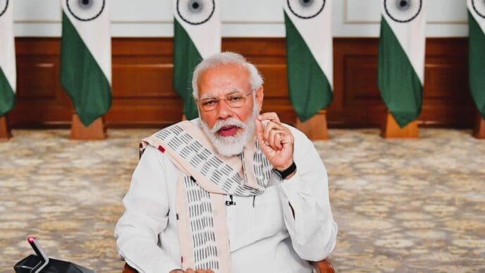 Indian Prime Minister Narendra Modi speaks while seated at a desk, with Indian flags in the background