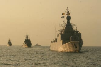 Four US military vessels sail in a line on the open sea under a hazy sky