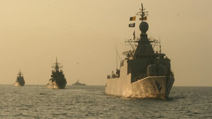 Four US military vessels sail in a line on the open sea under a hazy sky