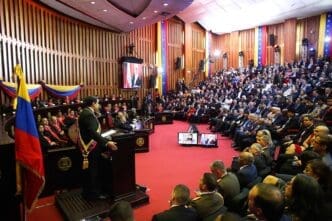 Nicolas Maduro, wearing a presidential sash, stands at a podium in a large, red-carpeted chamber with a seated audience, as he is sworn in as president.