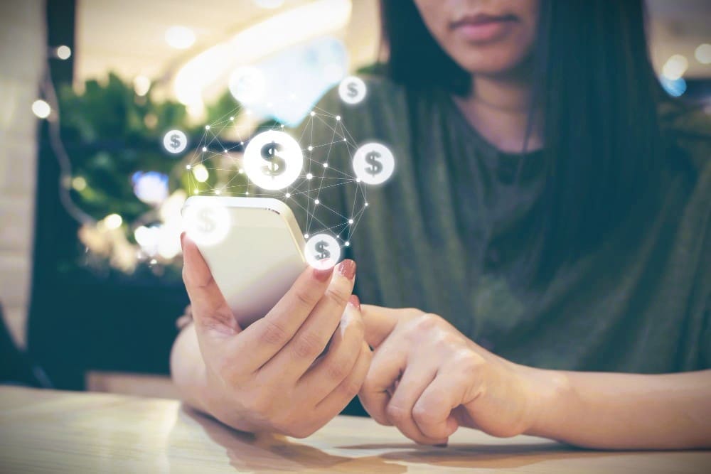 A person is holding a smartphone that has a digitally overlaid graphic of a network of glowing dollar signs connected by lines.