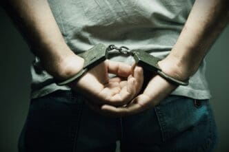 A person is shown from the back, wearing handcuffs with their hands behind them