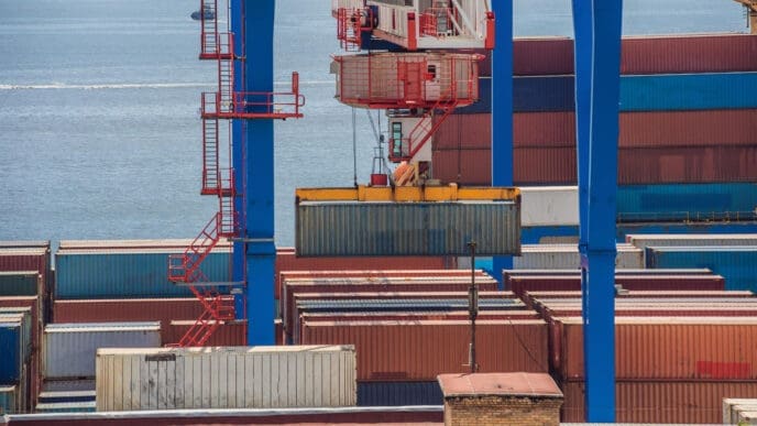 A port crane lifts a large shipping container over a field of stacked containers