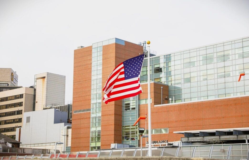 The American flag waves in front of a modern hospital or public health building
