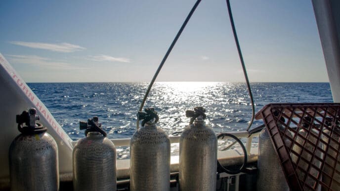 Four scuba tanks are secured on the deck of a boat, with the sun-drenched Florida ocean stretching into the distance.