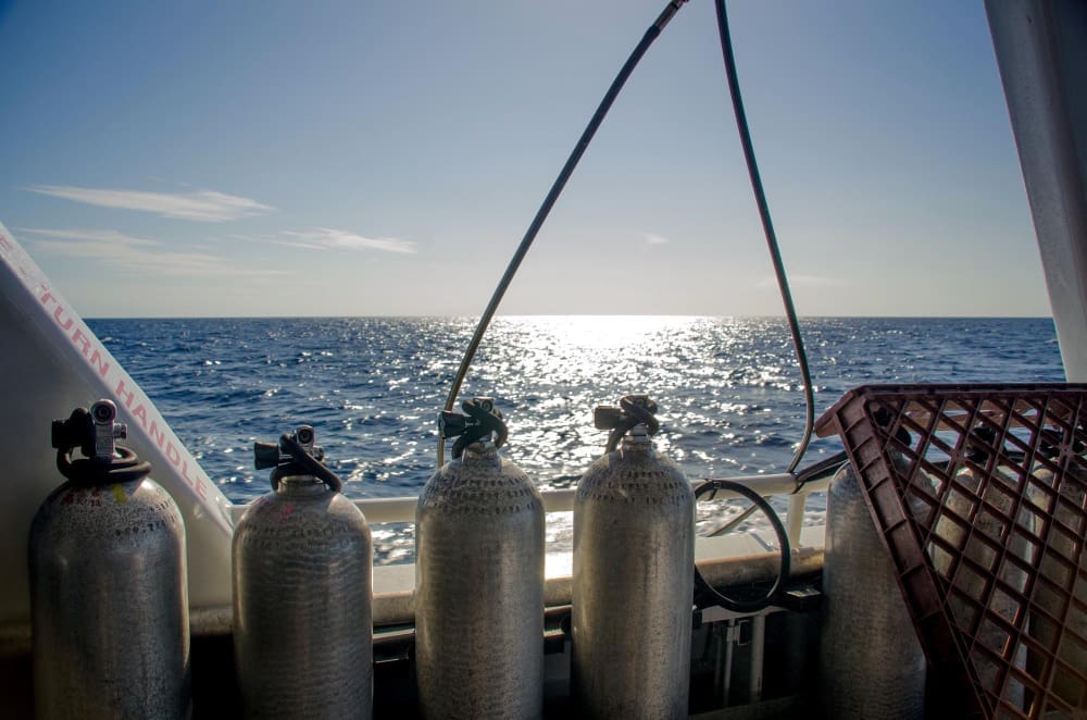 Four scuba tanks are secured on the deck of a boat, with the sun-drenched Florida ocean stretching into the distance.