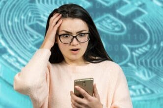 A young woman in glasses looks shocked and holds her head while looking at her phone
