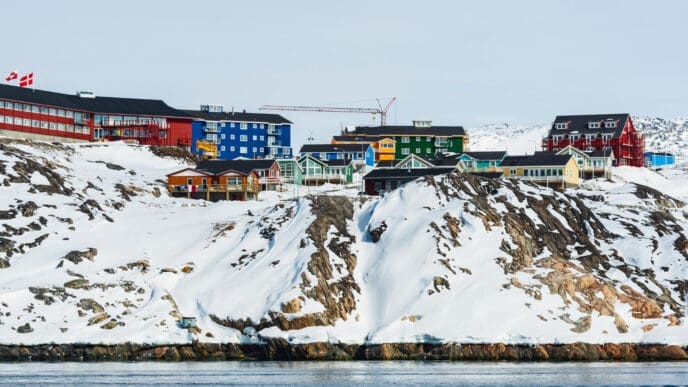 Colorful houses stand on a snow-covered rocky hillside next to a body of water in Sisimiut, Greenland