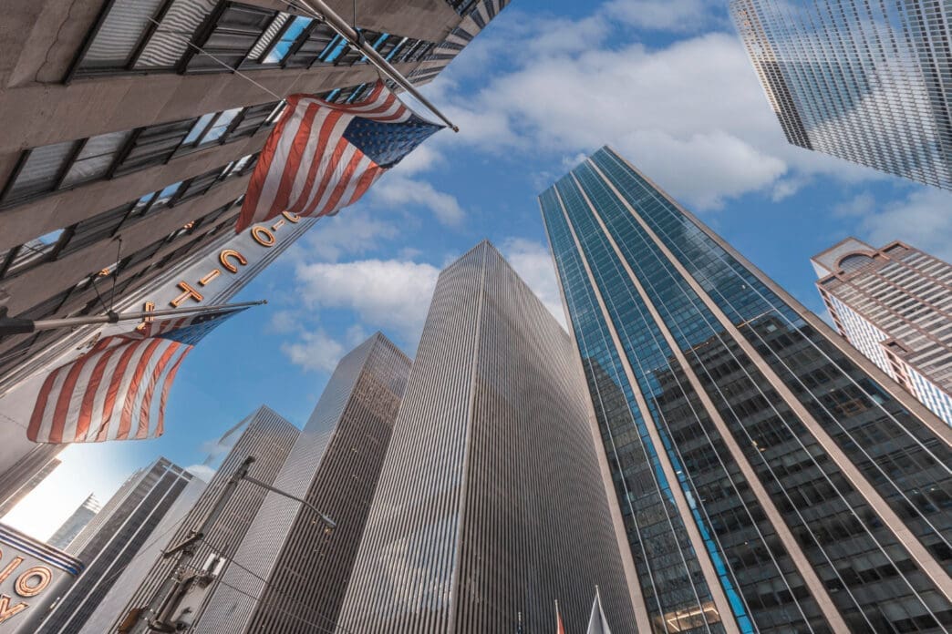 American flags hang from a skyscraper in Manhattan, with a low-angle view of other tall buildings