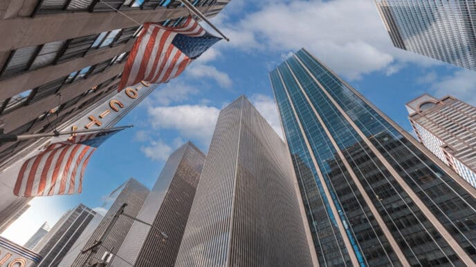 American flags hang from a skyscraper in Manhattan, with a low-angle view of other tall buildings