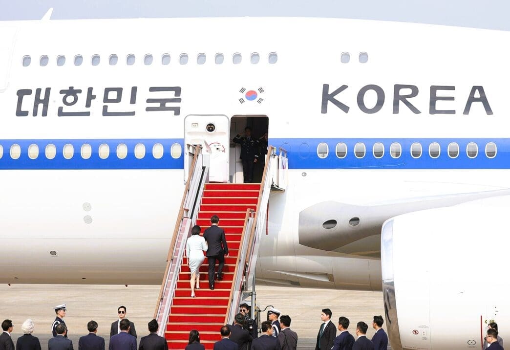 South Korean President Lee and his wife walk up a red carpeted staircase to board an airplane with "KOREA" written on its side.