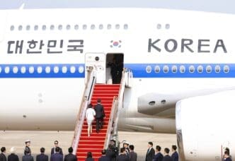 South Korean President Lee and his wife walk up a red carpeted staircase to board an airplane with "KOREA" written on its side.