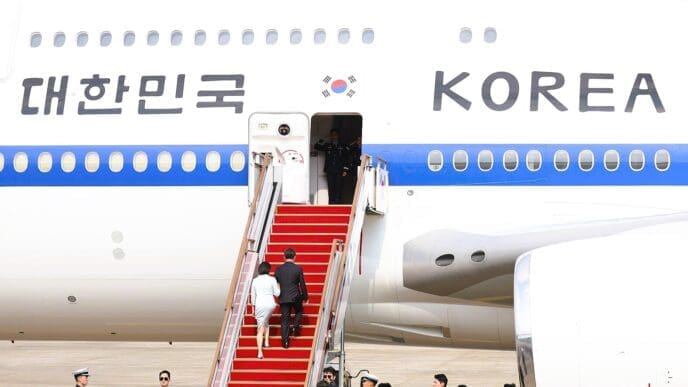 South Korean President Lee and his wife walk up a red carpeted staircase to board an airplane with "KOREA" written on its side.